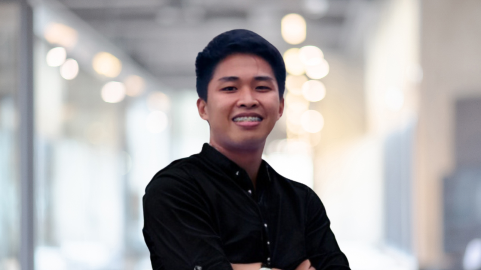 A man in a black shirt stands with his arms crossed in a blurred indoor setting, reflecting the dynamic spirit of Small World Marketing.