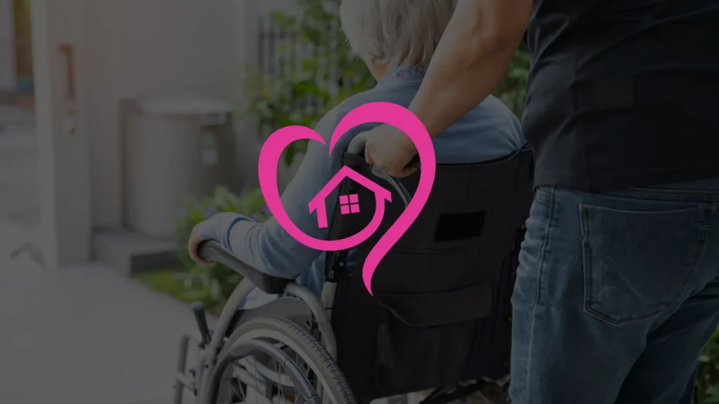 A person in a wheelchair is being pushed by a caregiver outdoors. A pink heart-shaped logo with a house inside is overlaid on the image, symbolizing home care or support services.