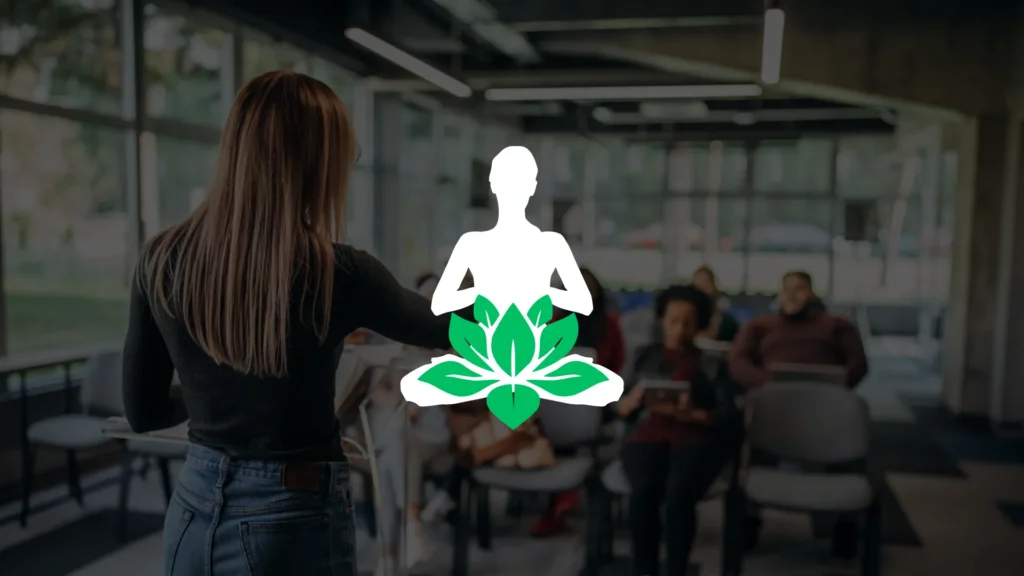 A woman stands in front of a seated audience in a classroom, with a white yoga pose and green lotus icon overlayed at the center of the image.