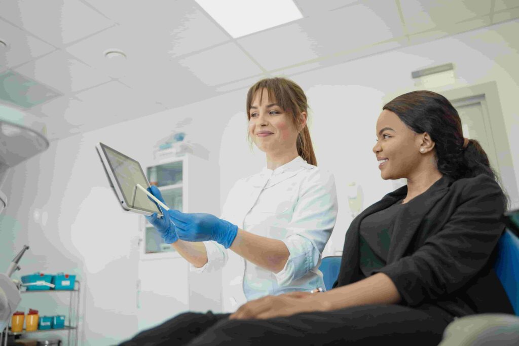 A healthcare professional wearing gloves shows a tablet to a smiling woman in a medical office, discussing information together—just like dentists might share Essential Local SEO Tips for Dentists in 2026 with their teams.
