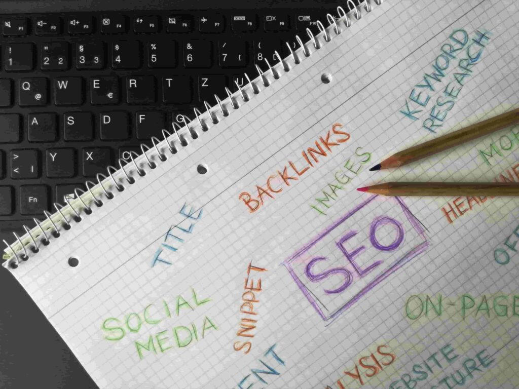 A spiral notebook featuring SEO terms like TITLE, BACKLINKS, and KEYWORD RESEARCH—key concepts for how family law firms can use SEO to attract new clients—sits on a black keyboard with two pencils resting on the page.